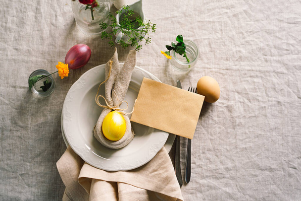 Счастливой Пасхи. Стильные пасхальные яйца на салфетке с весенними цветами на белом деревянном фоне. Накрываем стол. Концепция счастливого пасхального праздника. - Фото, изображение