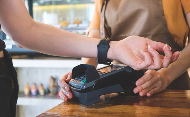Kobieta klient za pomocą smartwatch dla bezdotykowych płatności za jej zamówienie w kawiarni. Pojęcie płatności bezgotówkowych. - Zdjęcie, obraz