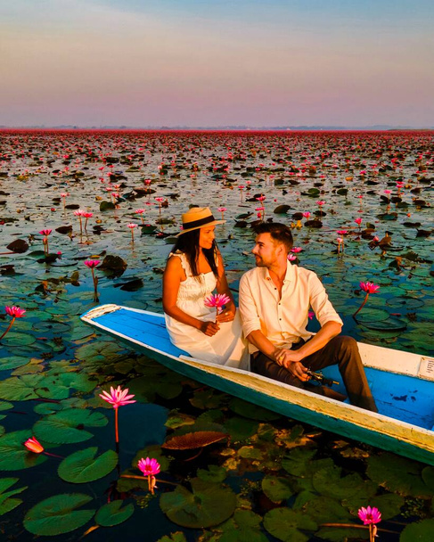 Sonnenaufgang am Meer aus rotem Lotus, Lake Nong Harn, Udon Thani, Thailand. Paar Männer und Frauen in einem Holzboot während des Sonnenaufgangs am Roten Lotussee in Thailand - Foto, Bild