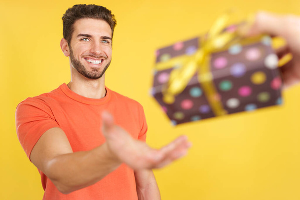 Happy caucasian man smiling while receiving a gift in studio with yellow background - Фото, изображение