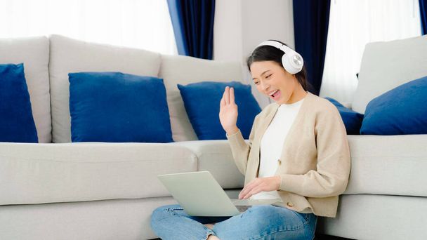 Egy fiatal ázsiai nő fejhallgatót visel, miközben számítógépen dolgozik a házban. Munka otthon, Videokonferencia, Videokonferencia, Diák tanulás online osztály - Fotó, kép
