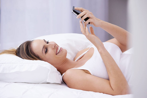 Časné ranní textové zprávy... Atraktivní mladá žena čtení textové zprávy při ležení v posteli - Fotografie, Obrázek