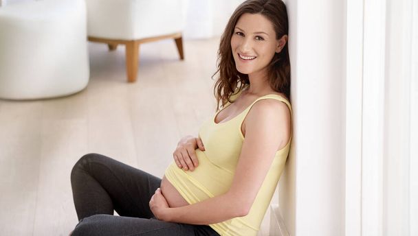Gentle beginings. a young pregnant woman sitting on her living room floor - Fotó, kép