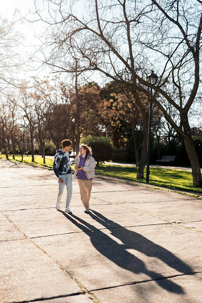 Stock photo of happy friends talking and using phone while walking in the park. - 写真・画像