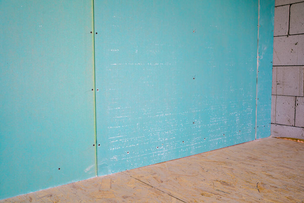Ανθεκτικός στην υγρασία τοίχος από γυψοσανίδες. Το εσωτερικό χώρισμα σε ένα ιδιωτικό σπίτι είναι καλυμμένο με μπλε γυψοσανίδα. Δωμάτιο με γυμνούς τοίχους και ισόγειο χωρίς επισκευή - Φωτογραφία, εικόνα