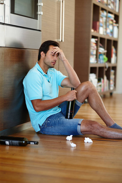 Ahogando sus penas. un hombre llorando bebiendo vino mientras está sentado en el suelo con algunos pañuelos - Foto, Imagen