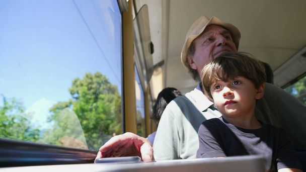 Il nonno fotografa il paesaggio mentre viaggia in treno con il nipote in grembo. Persona anziana fotografare scenario sul trasporto in movimento - Foto, immagini