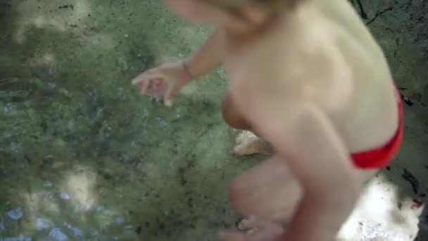 Çocuk suya atlıyor yalın ayak sıçrıyor. Çamur göletinde oynayan küçük çocuğun tasasız çocukluk anı. - Video, Çekim