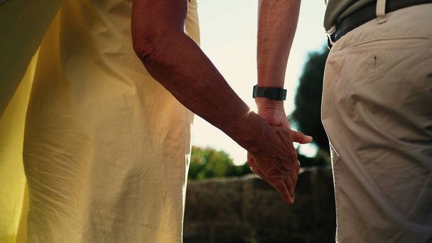 Rücken zweier älterer Menschen, die sich im Sonnenlicht im Freien an den Händen halten. Seniorenpaar mit zusammengehaltener Hand. Resilienz Liebe und Unterstützung Konzept - Foto, Bild