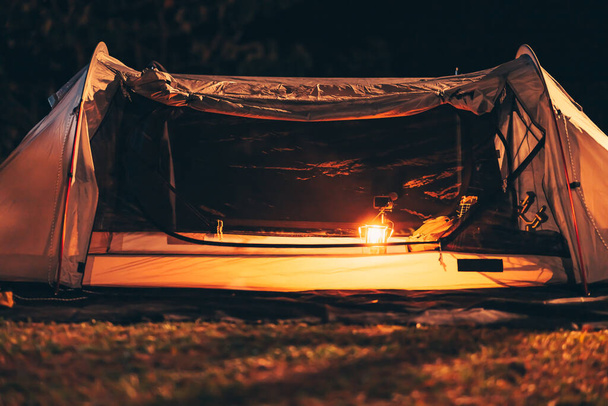 Een gaslamp staat 's nachts op de tentvloer en een tas met een ukelele en schoenen ernaast. Kampeeruitrusting, roeping en reisconcept. - Foto, afbeelding