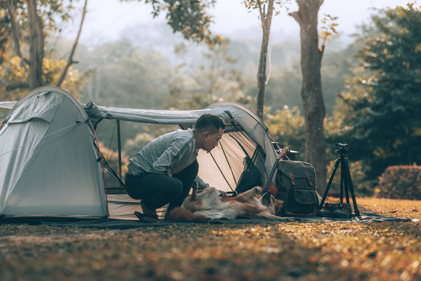 Man playing with dog in the morning during a camping trip in the forest on holiday. Vocation and travel concept. - Photo, image