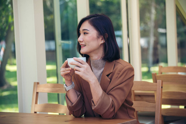 Donna di bellezza che beve caffè nero in caffetteria con tazza di freschezza. Amante del caffè. Asiatico donna bere caffè nero mano in possesso di tazza al caffè giardino verde. Giovane donna sorriso faccia amore bere caffè - Foto, immagini