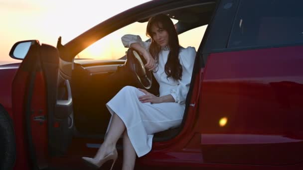 Femme heureuse en robe blanche dans une voiture rouge au coucher du soleil - Séquence, vidéo