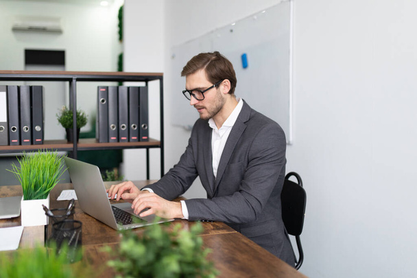 atraente advogado masculino estudando informações olhando para laptop enquanto sentado no escritório. - Foto, Imagem
