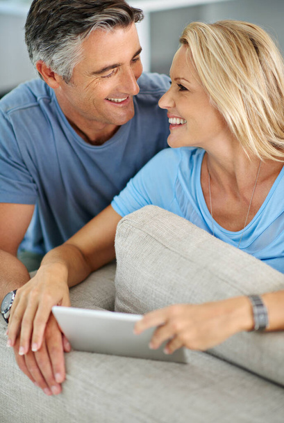 Compartir un poco de risa en línea. una pareja sonriente sentada en casa usando una tableta digital - Foto, imagen