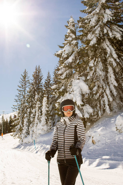 Jeune femme profitant de la journée hivernale de ski sur les pistes enneigées, entourée de grands arbres et habillée pour le froid - Photo, image