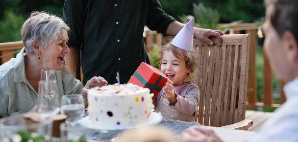 A multi generation family celebratiing birthday of little girl and having garden party outside on patio. - Fotó, kép
