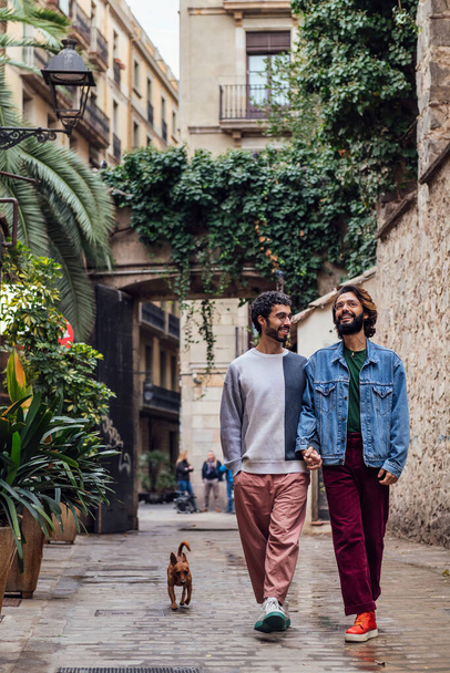 gay male couple walking with his dog along a beautiful ancient street decorated with plants, concept of leisure and love between people of the same sex - Fotó, kép