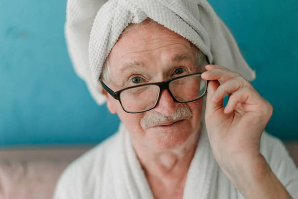 Happy senior man in glasses sitting at sofa in bathrobes and looking at camera. - Photo, image