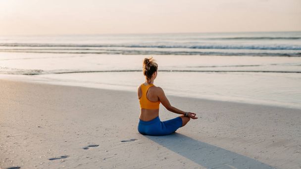 Vista trasera de la mujer joven haciendo ejercicios en la playa, rutina de la mañana y el concepto de estilo de vida saludable. - Foto, imagen