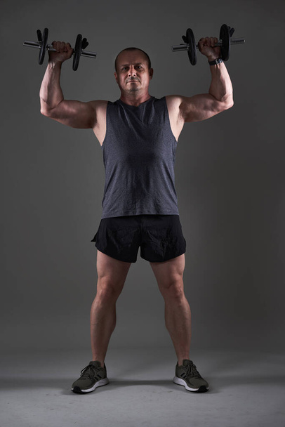 Full body shot of a mature man doing a fitness workout on gray background - Fotó, kép