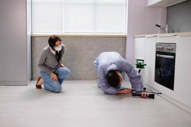 Mulher olhando para exterminador trabalhador pulverizador inseticida químico para controle de pragas de cupins na cozinha da casa
 - Foto, Imagem