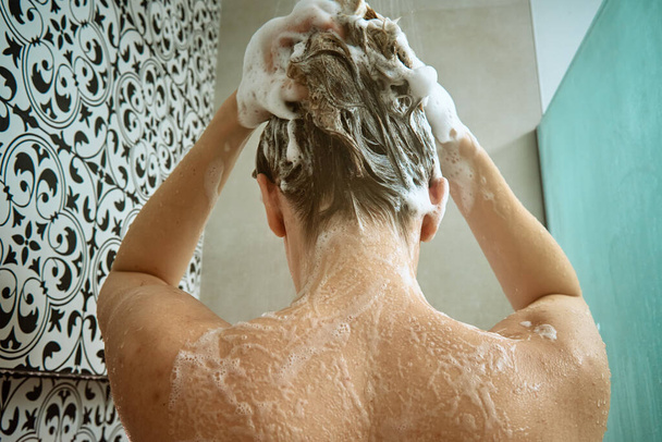Widok nagich kobiet biorących prysznic w kabinach prysznicowych. Kobieta myjąca włosy w łazience. Poranna higiena - Zdjęcie, obraz