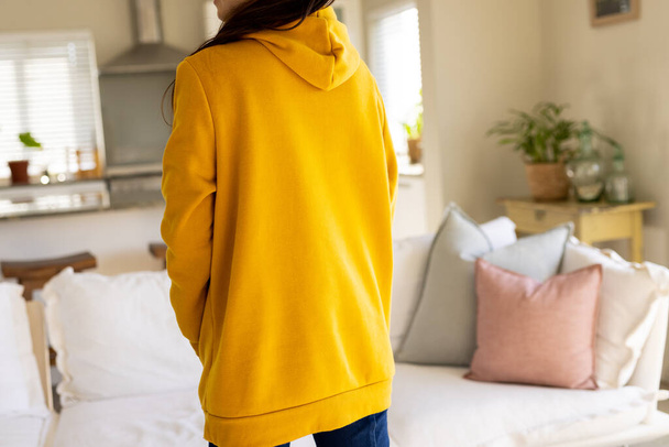 Biracial woman wearing yellow sweatshirt with copy space in living room. Fashion, design, color and clothes concept. - Foto, afbeelding