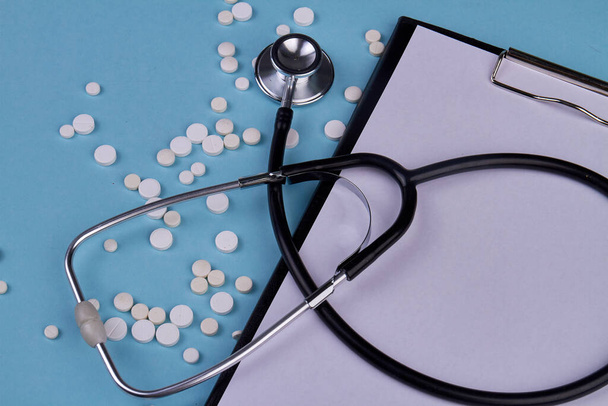 Close up stethoscope with clipboard and white pills. Blank paper for copy space. - Foto, Imagen
