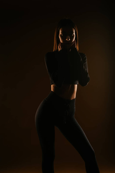 Молода приваблива дівчина в чорному спортивному одязі торкається шиї
 - Фото, зображення