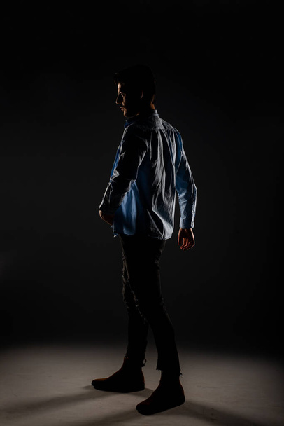 Vista lateral de un guapo modelo quitándose la camisa y posando dentro del estudio - Foto, Imagen