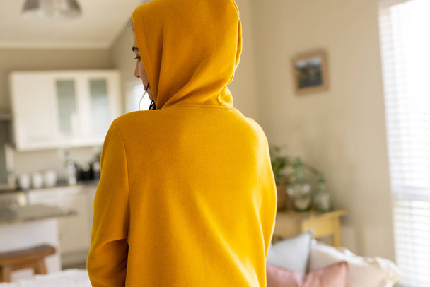 Biraciale vrouw draagt gele sweater met kopieerruimte in de woonkamer. Mode, design, kleur en kleding concept. - Foto, afbeelding