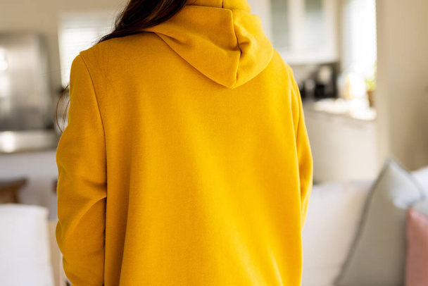 Midsection of biracial woman wearing yellow sweatshirt with copy space in living room. Fashion, design, color and clothes concept. - Foto, afbeelding