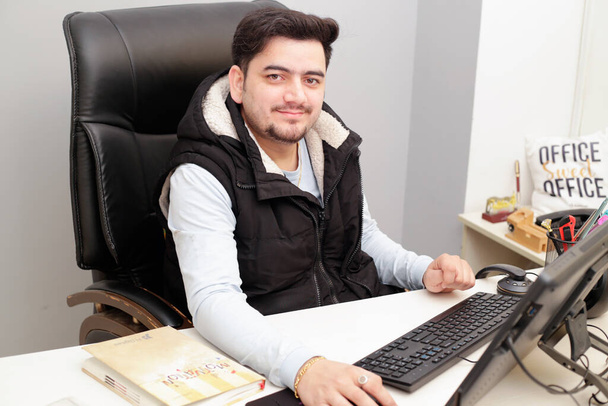Ein junger Geschäftsmann sitzt im Büro und arbeitet am Computer.  - Foto, Bild