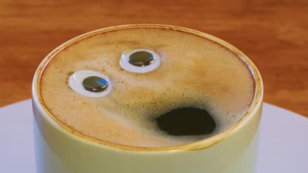 Smiling coffee man in a cup. Fragrant, lively coffee with eyes and mouth. Human face on fresh, milky coffee crema. High quality 4k footage - Πλάνα, βίντεο