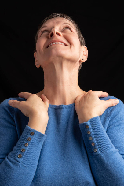 Studioaufnahme einer lächelnden Frau mit dem Rücken zum Gesicht und den Händen auf den Schultern, mit kurzen Haaren und einem blauen Pullover mit Manschettenknöpfen - Foto, Bild