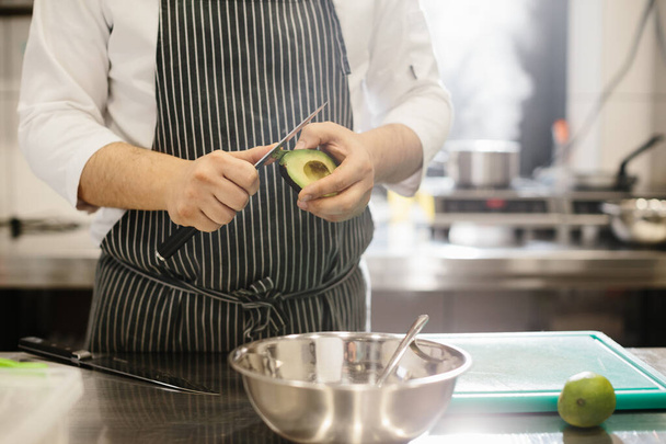 Šéfkuchař připravuje jídlo. Detailní záběr kuchaře, jak loupá avokádo. - Fotografie, Obrázek