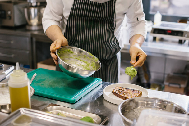 Ο σεφ ετοιμάζει φαγητό. Κοντινό πλάνο ενός αρσενικού σεφ προετοιμασία τοστ αβοκάντο σε μια ευρύχωρη σύγχρονη κουζίνα. - Φωτογραφία, εικόνα