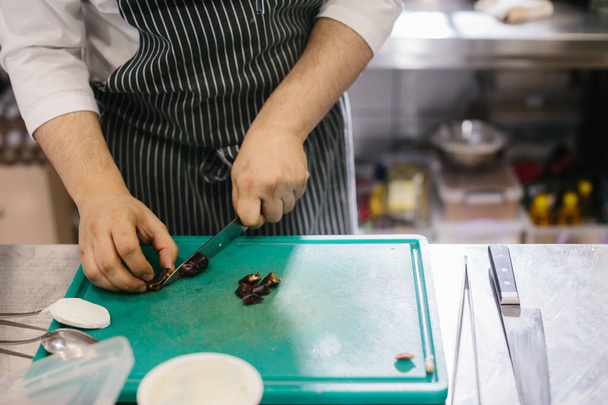 Het proces van het maken van muesli in een restaurant, de mannelijke chef snijdt data in de keuken. - Foto, afbeelding