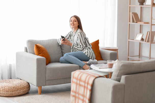 Mladá žena pomocí mobilního telefonu na šedé pohovce doma - Fotografie, Obrázek
