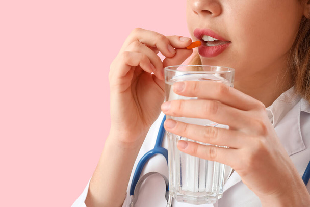 Beautiful doctor with vitamin supplement and glass of water on pink background, closeup - Фото, зображення