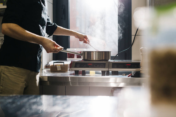 The cook works with an induction hob. The process of frying or stewing close-up. - Photo, image