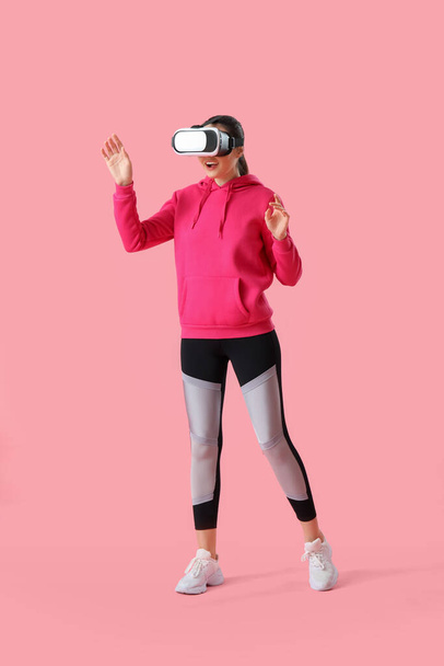 Sporty young woman in VR glasses on pink background - Foto, immagini