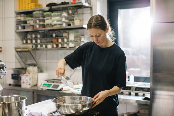 Een vrouwelijke kok werkt in een moderne industriële keuken. Het proces van het maken van taarten in een bakkerij of café. - Foto, afbeelding