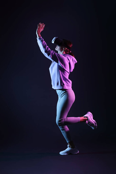Pretty young woman in VR glasses throwing virtual ball on black background - 写真・画像