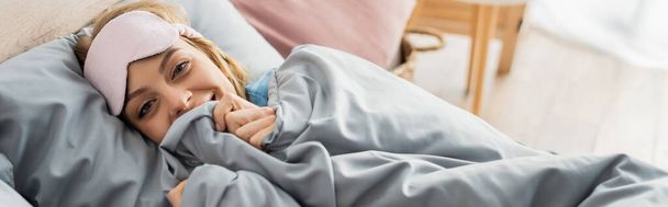 happy young woman in sleeping mask lying under blanket in comfortable bed, banner  - Fotografie, Obrázek