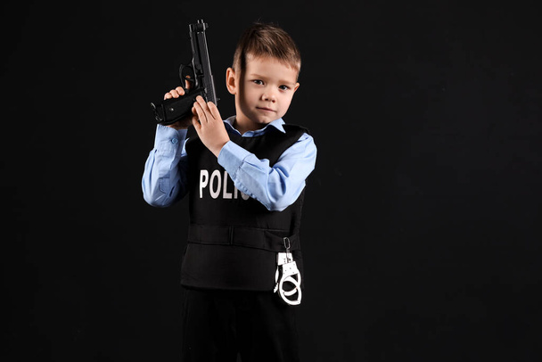 Cute little police officer with gun on black background - Fotografie, Obrázek