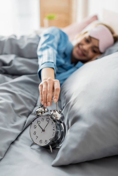 mujer feliz tomando despertador retro mientras está acostado en la cama por la mañana  - Foto, Imagen