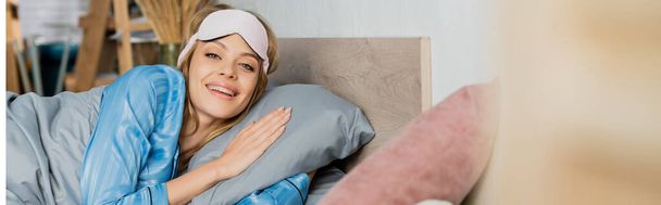 веселая женщина в маске для сна и голубой пижаме, лежащей в постели, баннер  - Фото, изображение