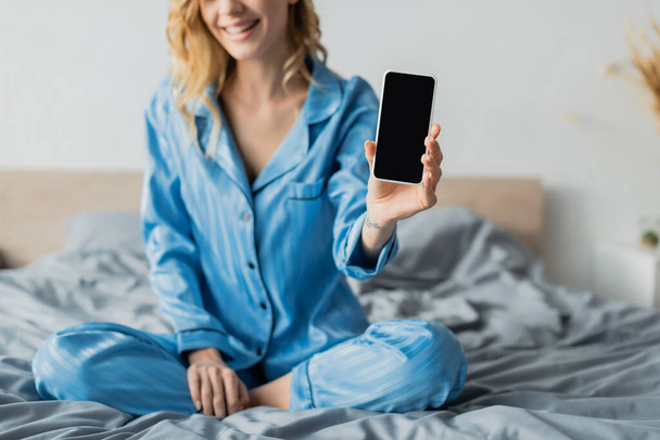 cropped view of pleased woman in blue pajama holding smartphone with blank screen  - Valokuva, kuva